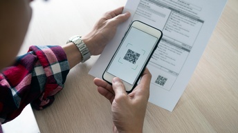 Person scannt einen QR Code von einem Dokument aus Papier mit dem Smartphone