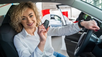Lächelnde Person sitzt am Steuer eines PKWs und hält Autoschlüssel in der Hand