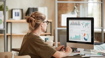 Person mit Brillen sitzt vor Computermonitor mit Diagrammen