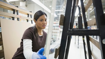Eine Person mit Handschuhen schiebt eingepackte Glasscheiben durch eine Werkstatt