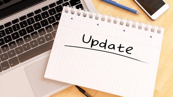 Notizblock mit Schriftzug Update liegt auf Computertastatur, daneben Stifte und ein Smartphone