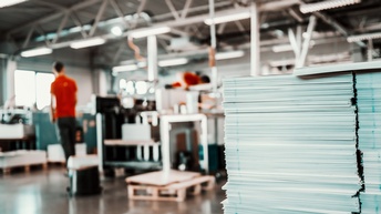 Mehrere Druckbögen aufeinander gestapelt, im Hintergrund Druckereihalle