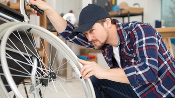 Person mit Kappe inspiziert Rad eines Rollstuhles