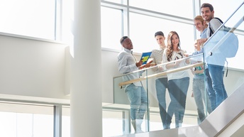 Gruppe junger Personen in gläsernem, hellem Stiegenhaus stehend