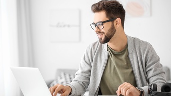 Person mit Brille und Bart blickt auf aufgeklapptes Notebook