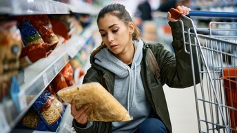 Person mit langen geschlossenen Haaren, Pullover und Jacke kauft Lebensmittle in einem Supermarkt ein