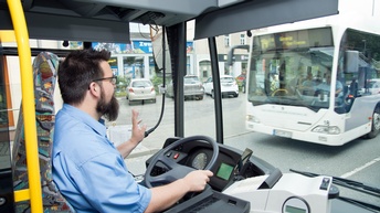 Person am Lenkrad eines Autobusses sitzend winkt anderem Autobus