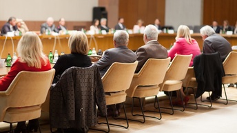 Rückenansicht mehrerer Personen, die an großem Konferenztisch sitzen
