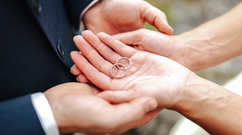 Zwei Personen halten die Hände zusammen, in der obersten Hand liegen zwei Ringe