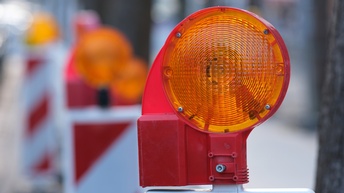 Nahaufnahme einer orangen Warnleuchte an einer Baustelle. Im Hintergrund stehen weitere Warnleuchten