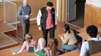Mehrere jugendliche Personen befinden sich in einem Lernraum während vorne eine Lehrperson freudig mit einem Tablet steht