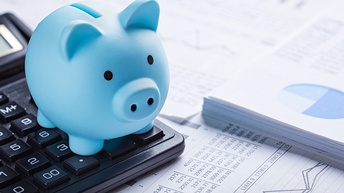 Blaues Sparschwein steht auf einem Taschenrechner neben verschiedenen Unterlagen mit Zahlen, Diagrammen und Kurven