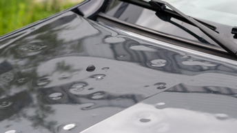 Nahaufnahme der Motorhaube eines dunklen PKWs, in der mehrere, kleine, runde Dellen sind
