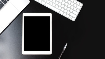 Mock-up von einem Tablett auf einem schwarzen Untergrund neben einem Laptop, einer Tastatur sowie einem Kugelschreiber, Topshot