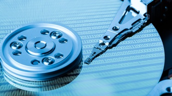 Nahaufnahme von einer Festplatte mit Schreibkopf und viele Ziffern mit 0 sowie 1 auf der Schreibplatte projiziert