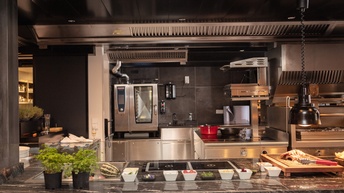 Küche eines Gastronomiebetriebes mit Edelstahlverkleidungen, ringsum Schälchen mit Zutaten stehend und Küchenzubehör