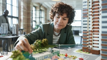Person in Businesskleidung arbeitet an einem Ausschnitt eines Modells mit Wohnbau- und Grünanlagen
