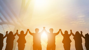 Mehrere Personen stehen in einer Reihe und halten sich an den Händen während sie in den Himmel bei Sonnenuntergang blicken, Konzept Teamgeist