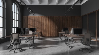 Hoher, großer Raum mit großen Fenstern, in dem Schreibtische, Stühle und Bildschirme stehen