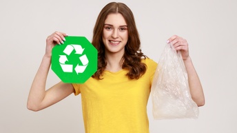 Portrait einer lächelnden Person in gelbem T-Shirt, die in einer Hand Recyclingzeichen - drei weiße im Kreis verlaufenden Pfeile auf weißem Hintergrund - und in anderer Hand Plastiksack hält