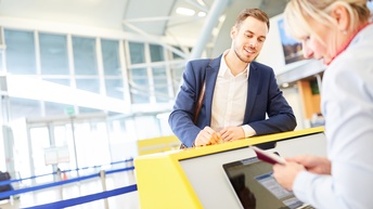 Lächelnde Person beugt sich über gelben Schalter zu Person verschwommen im Vordergrund, die Pass kontrolliert