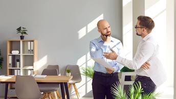 Zwei Männer in Hemden verhandeln stehend im Büro an einer Fensterbank