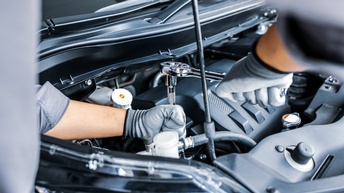 Nahaufnahme einer Person mit Handschuhen, die in der geöffneten Motorhaube eines Autos mit einer Zange handwerkt