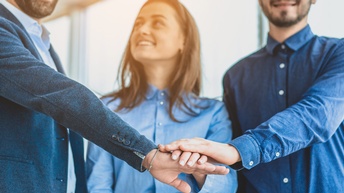 Drei Personen stehen gemeinsam und reichen die Hände vor ihnen zusammen