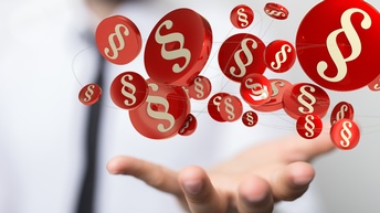 Nahaufnahme der linken Hand einer Person, die nach oben geöffnet ist. Über der Hand sind mehrere rote Kreise als 3D-Form. In jedem Kreis ist ein helles Paragrafenzeichen. Die Kreise sind durch schmale Fäden miteinander verbunden