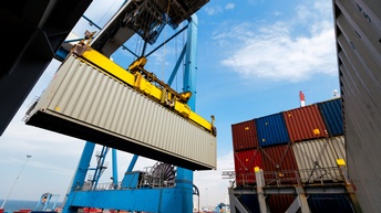 Ein Container wird von einem Kran angehoben, ringsum stehen viele weitere Container