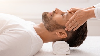 Nahaufnahme von einer Person mit geschlossenen Augen, braunem kurzen Haar und Bart, die gerade am Kopf massiert wird