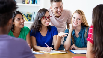 Eine Personengruppe sitzt gemeinsam an einem Tisch an der Uni und bereitet sich für Prüfungen vor.