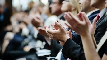 Seitliche Aufnahme eines Publikums in Sakkos, das in die Hände klatscht