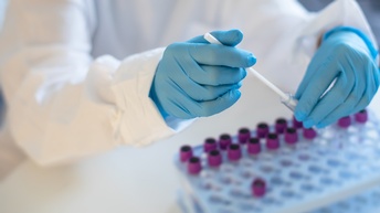 Hände mit blauen Gummihandschuhen halten Covid-19-Tests-Glasröhrchen