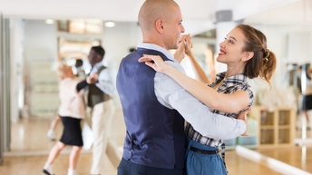 Seitliche Aufnahme zweier sehr nach sich gegenüber stehender Personen, die sich anblicken und auf der einen Seite sich an den Händen halten und auf der anderen die Arme auf dem Körper der anderen Person haben