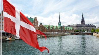 Die dänische Flagge weht im Wind, im Hintergrund eine Stadtansicht.