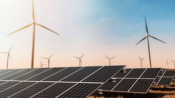 Feld im Sonnenuntergang: Im Vordergrund Solarpaneele, im Hintergrund Windräder