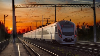Ein grauer Zug fährt auf Schienen. Die Lichter an einer Seite leuchten rötlich. Neben den Schienen sind weitere Gleise. Über ihnen verlaufen Kabel. Der Himmel ist rötlich. Die Sonne steht tief.