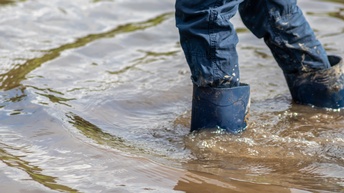 Person in Jeans geht mit blauen Gummistiefeln in tiefem Wasser, Hochwasser