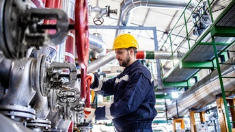 Person in Schutzbekleidung mit Schutzhelm arbeitet in einer Raffinerie
