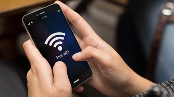 Nahaufnahme der Hände einer Person, die ein Smartphone hält, auf dessen Bildschirm ein Wlan-Symbol ist. Darunter steht free wifi