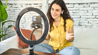 Eine Person sitzt vor einem Ringlicht und nimmt mit dem Smartphone ein Video auf.