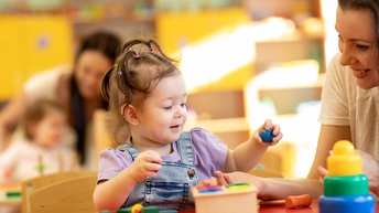 Kind spielt mit Klötzen, beisitzend lächelnde Person