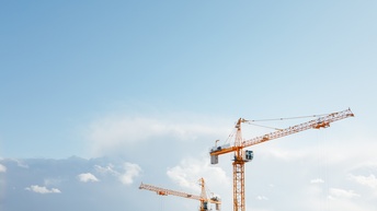 Zwei hohe, gelbe Kräne mit Fahrerkabinen vor blauem Himmel