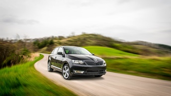Schwarzes Auto fährt auf Landstraße umgeben von grünen Wiesen in Bewegungsunschärfe