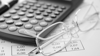 Detailansicht Brille neben Taschenrechner auf Papier mit Zahlen liegend