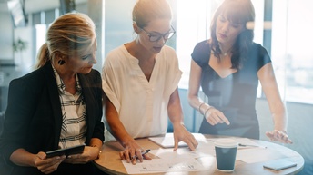 Personen in Businesskleidung stehen rund um einen Stehtisch und begutachten Unterlagen