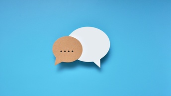 Auf blauem Hintergrund sind zwei Sprechblasen. Die linke Sprechblase sind braun. In ihr sind vier schwarze Punkte. Die rechte Sprechblase ist weiß und leer