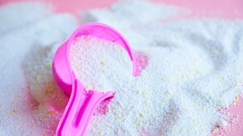 Nahaufnahme von Waschmittel in Pulverform mit einem rosa Messbecher auf einem rosafarbenen Untergrund