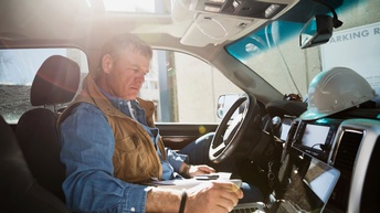 Person sitz auf Fahrersitz in Auto und bedient aufgeklappten Laptop